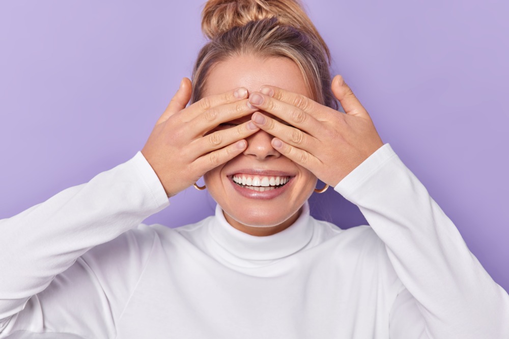 horizontal-shot-happy-european-woman-covers-eyes-with-hands-awaits-surprise-smiles-broadly-wears-casual-white-turtleneck-isolated-purple-background-waits-miracle-blind-concept-222